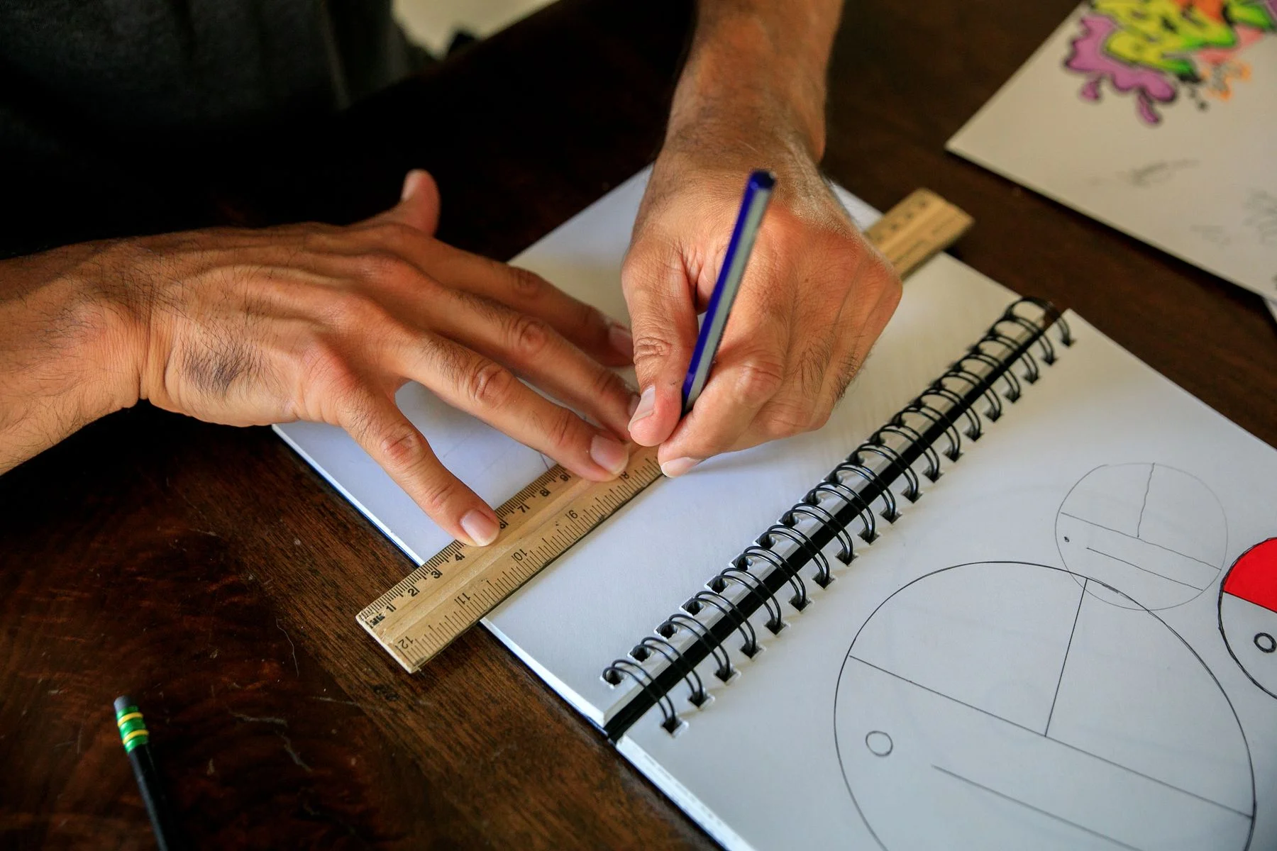 Hands drawing with a pencil and ruler in a notebook