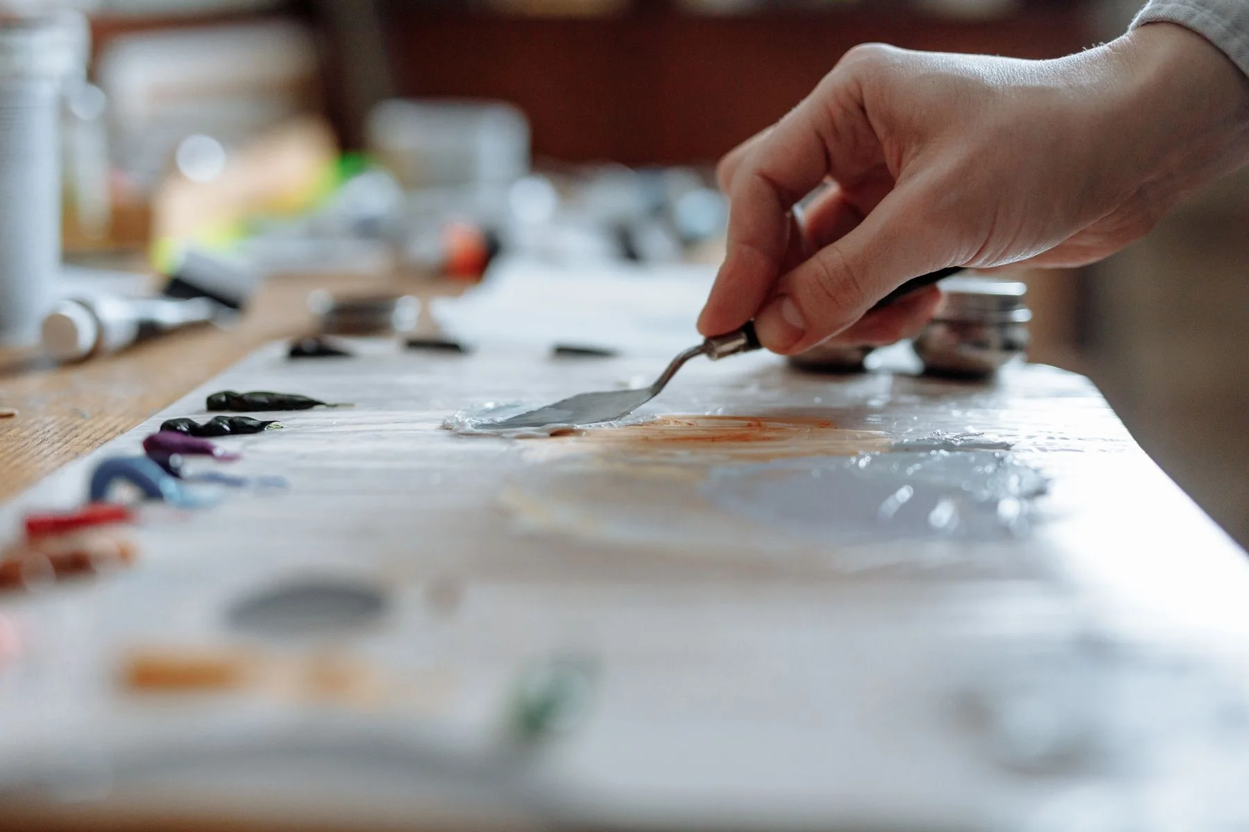 A hand mixing paint on a wooden artist’s palette