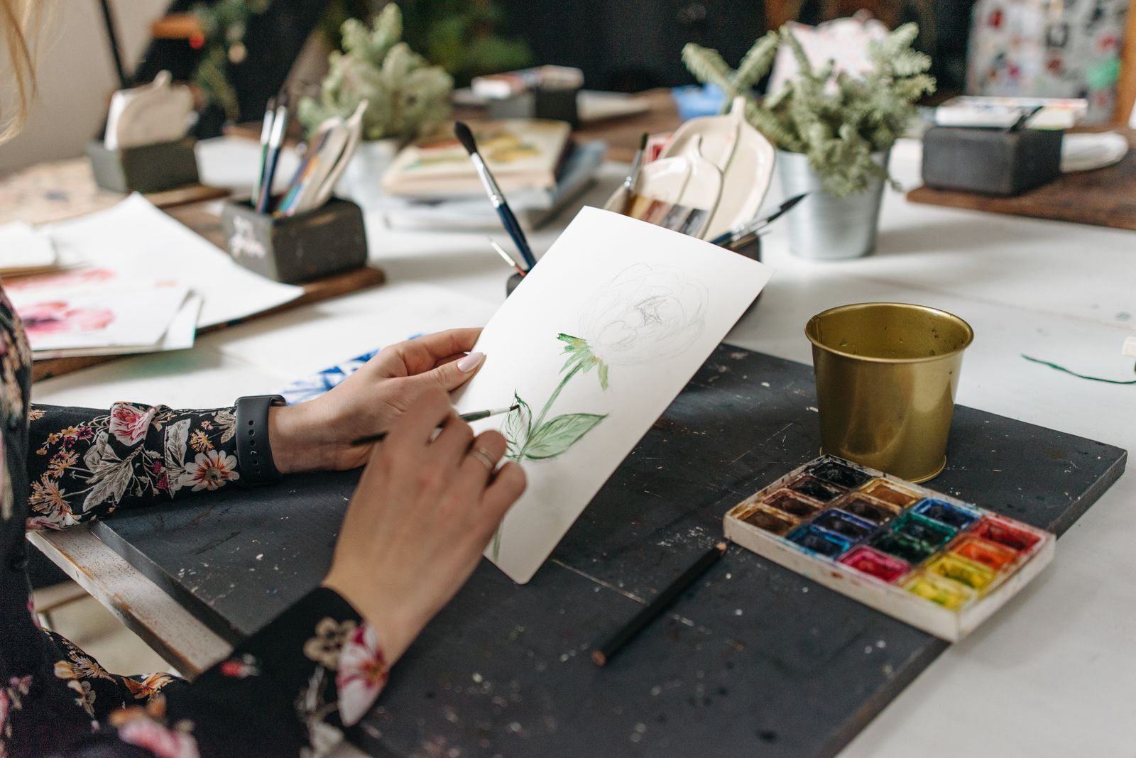 An artist working on a botanical watercolor with green leaves on white paper