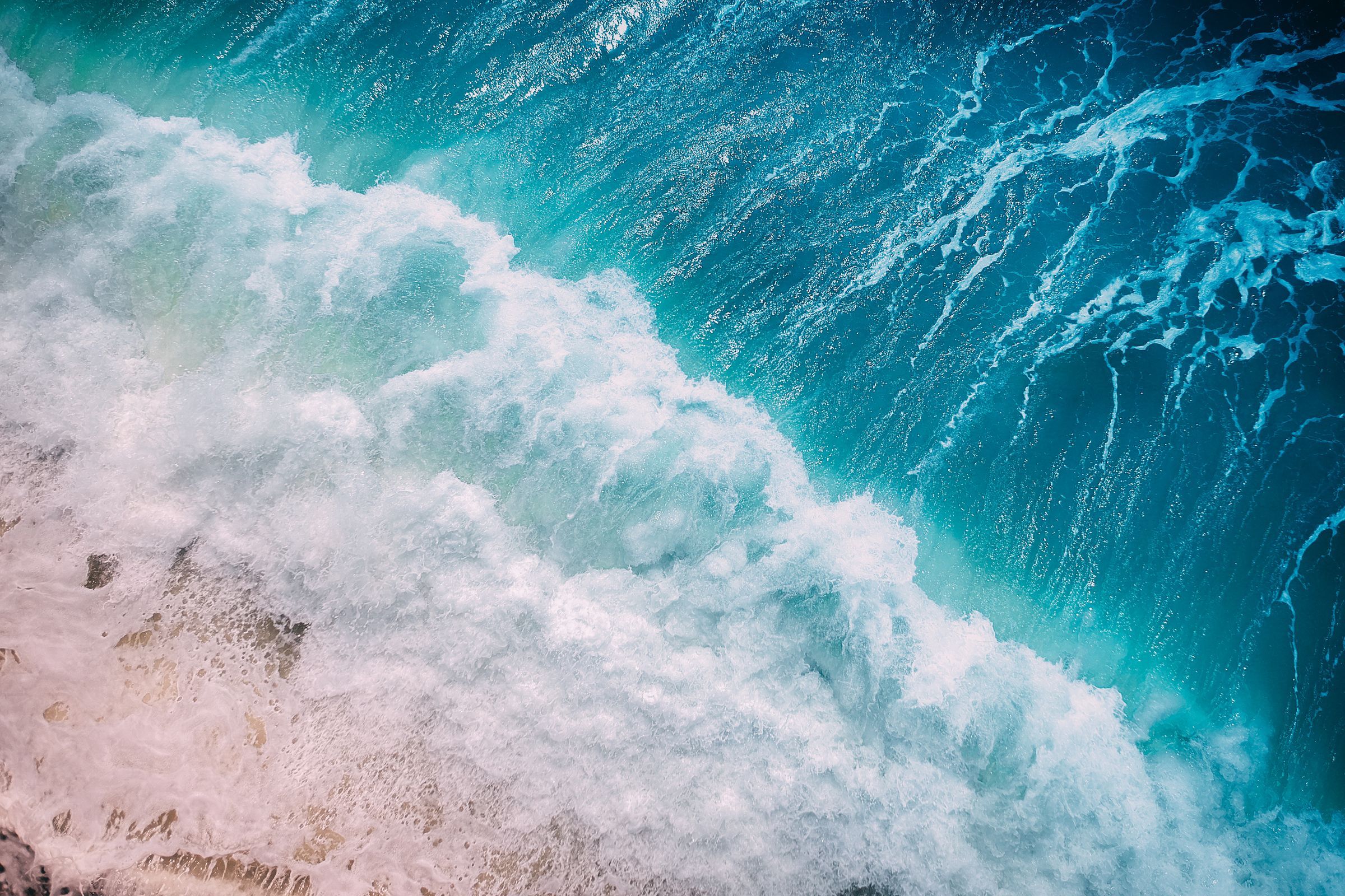 Turquoise ocean waves breaking into white foam from above